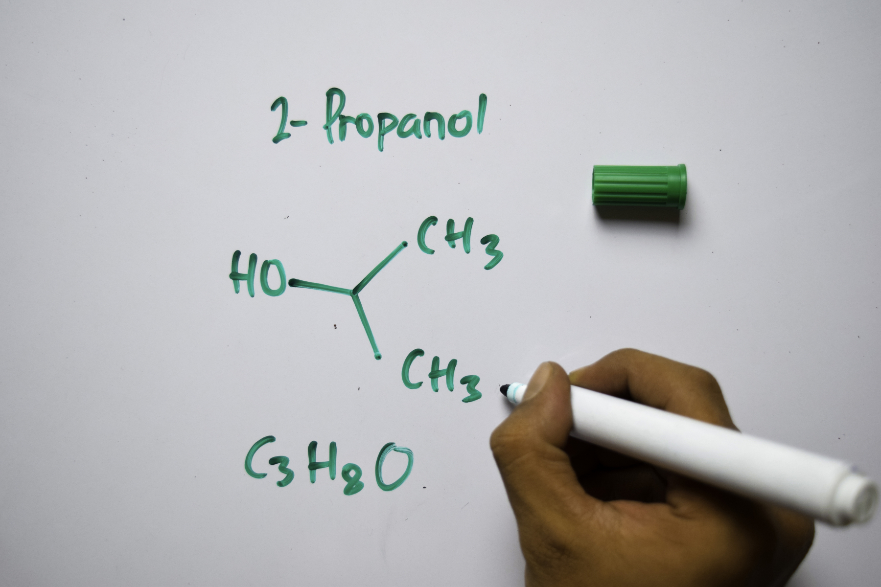 Hånd som skriver og tegner kjemiske formler for isopropanol på whiteboard