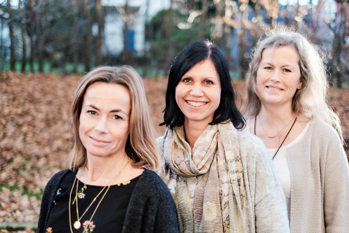 Tre smilende kvinner som ser i kameraet 