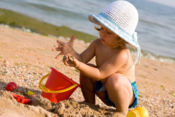 Barn med solhatt leker på stranden.