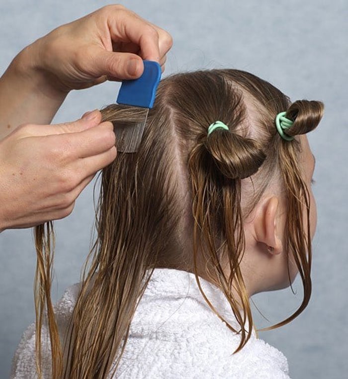 Barn får hjelp av voksen til å dele opp håret i flere hestehaler.