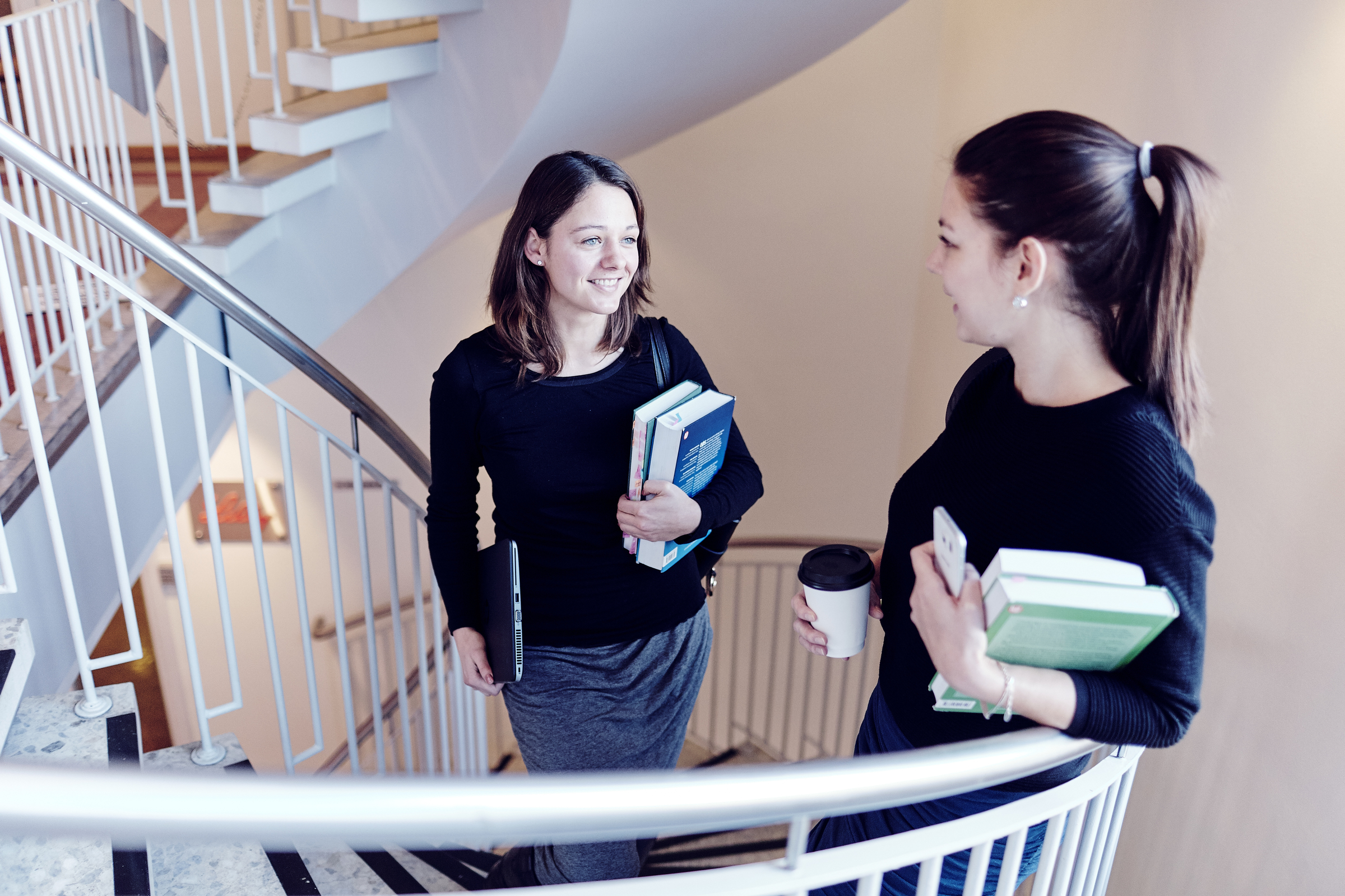 To unge kvinner som holder bøker, i en trapp