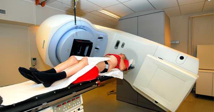 Pasient ligger foran en behandlingsmaskin og får strålebehandling.