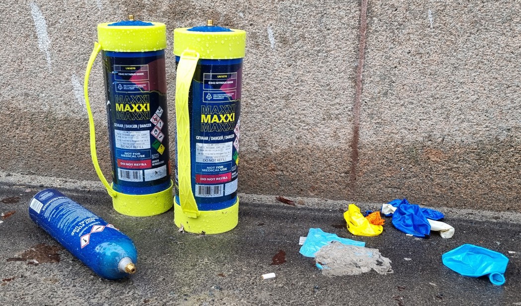 Empty nitrous oxide containers in the street against a wall