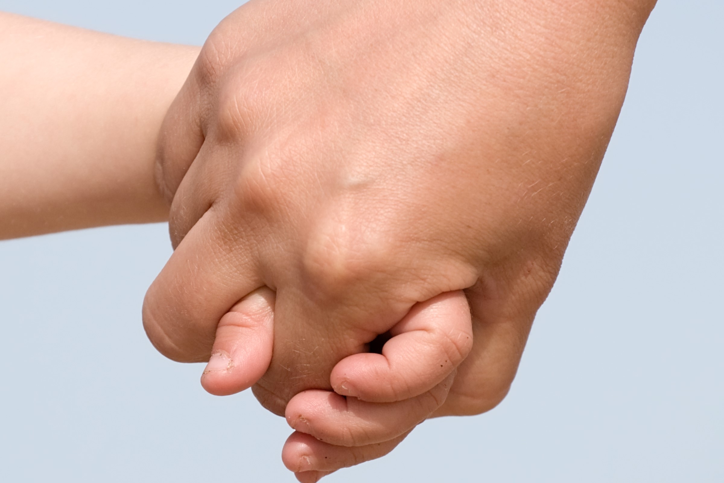 mother and child holding hands closeup on sky background