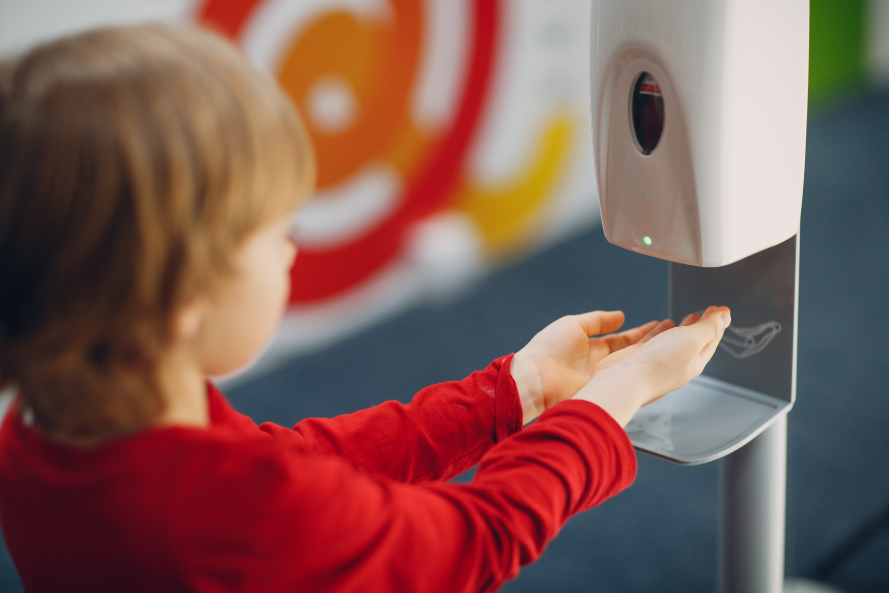 Barn med rød genser forsyner seg med håndsprit fra automatisk dispenser