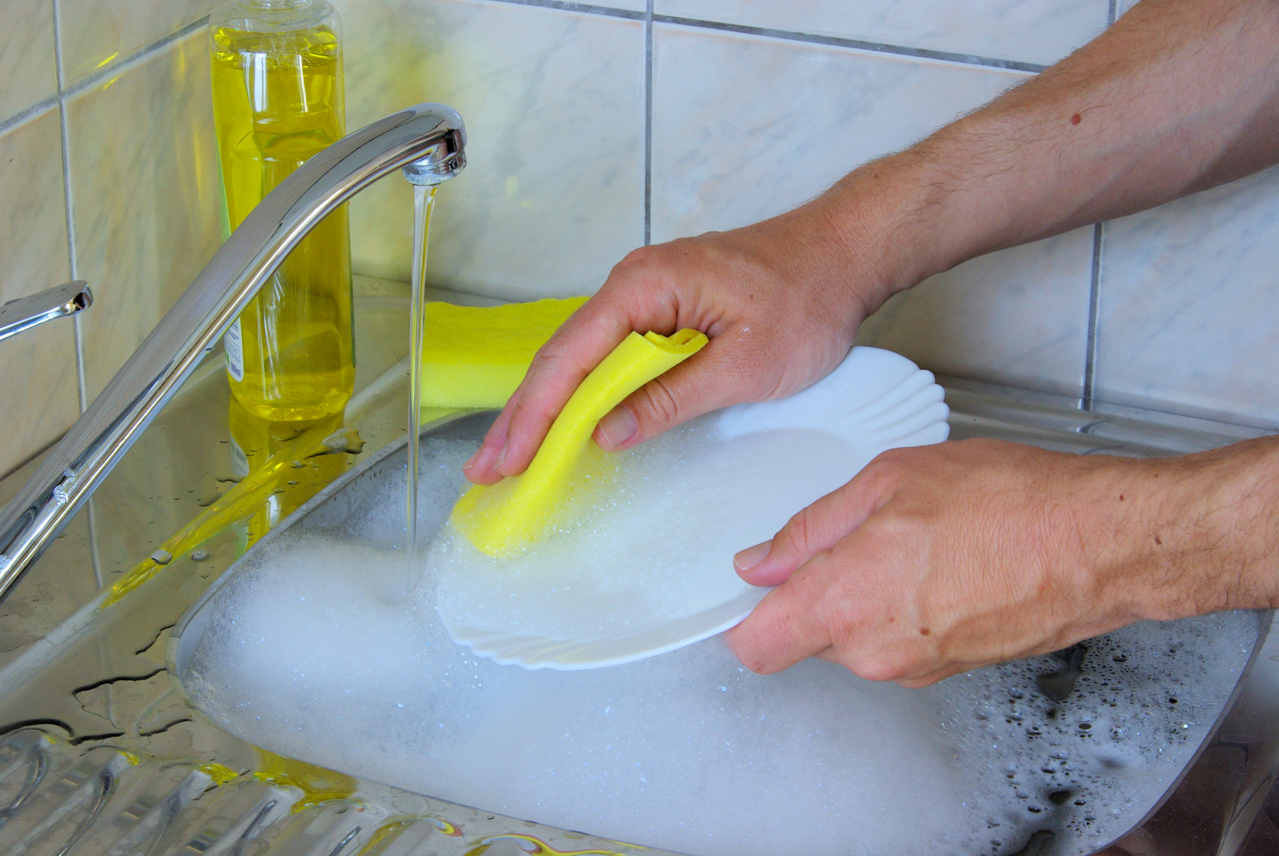 Håndoppvask av hvit tallerken med gul vaskeklut, gul såpeflaske i bakgrunnen