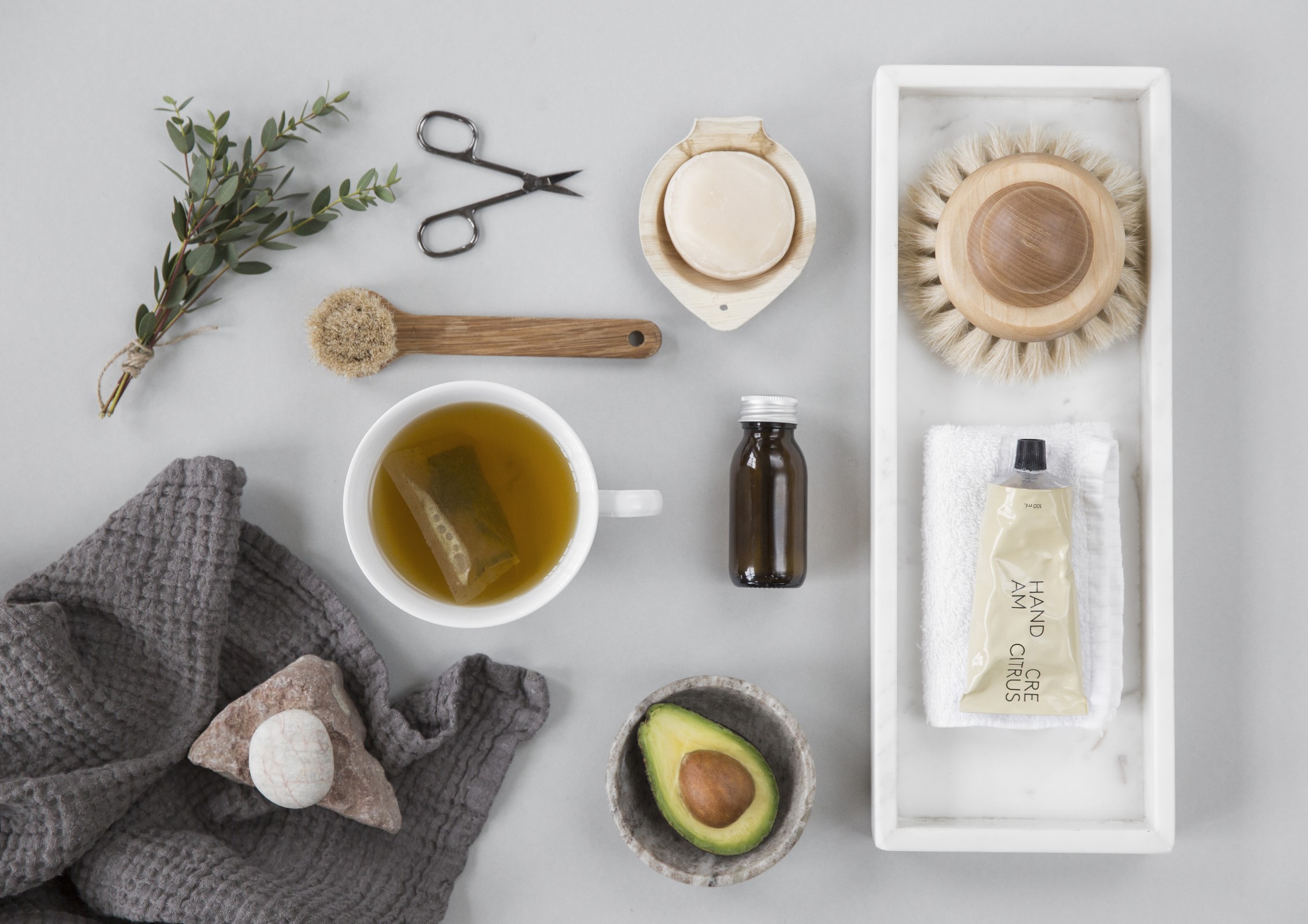 Bilde av kosmetikk og duftoljer, tekopp, krydderkvast, avocado i kopp, saks og håndkle med stein på.