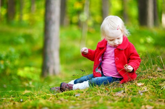 Et lite barn med fargerike klær som sitter på bakken i skogen og plukker sopp.