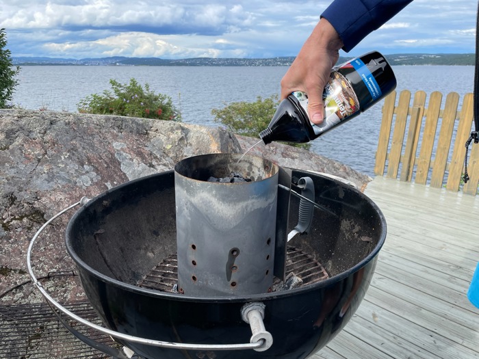 En mann heller på tennvæske på en kulegrill med grillkull.