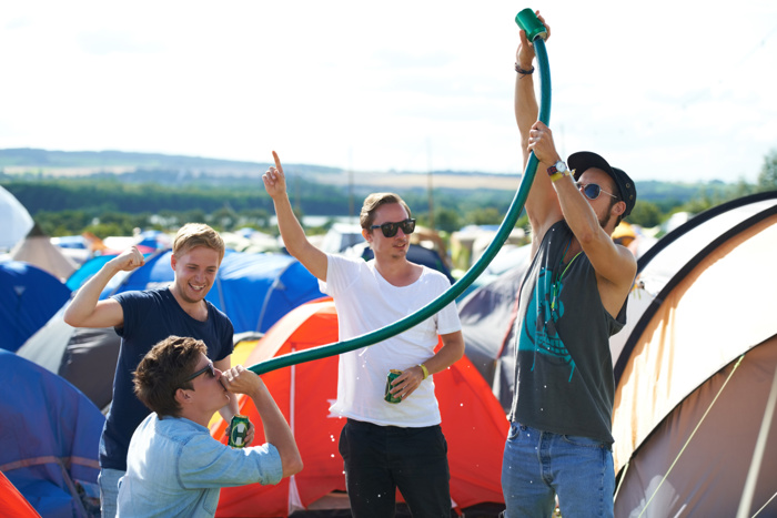 Personer på en campingplass drikker alkohol under et arrangement med telt i bakgrunnen.