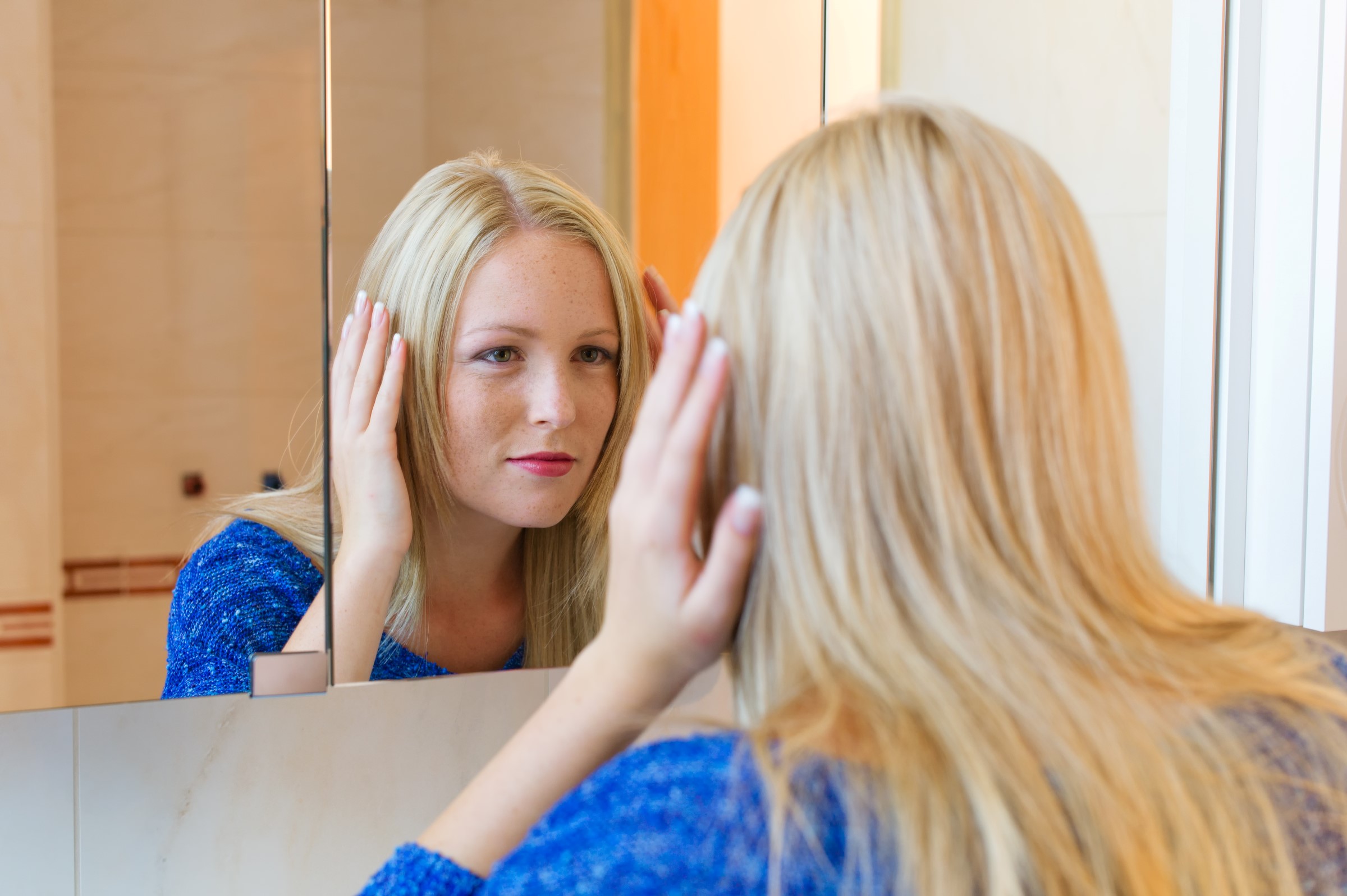 Bilde av en kvinne som ser i speilet og tar på håret sitt