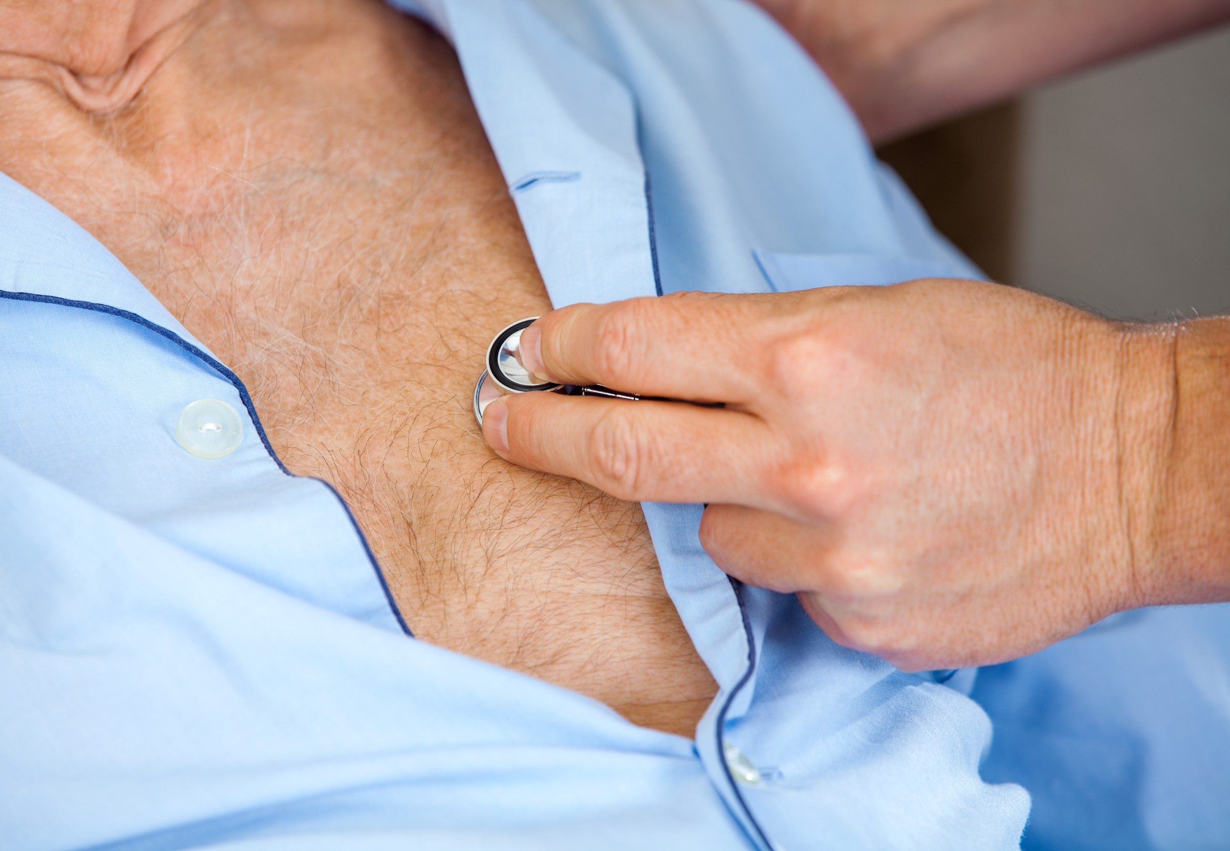 Cropped image of male caretaker examining senior man's chest with stethoscope at nursing home