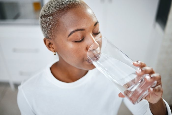 Kvinne i hvit genser som drikker fra ett vannglass