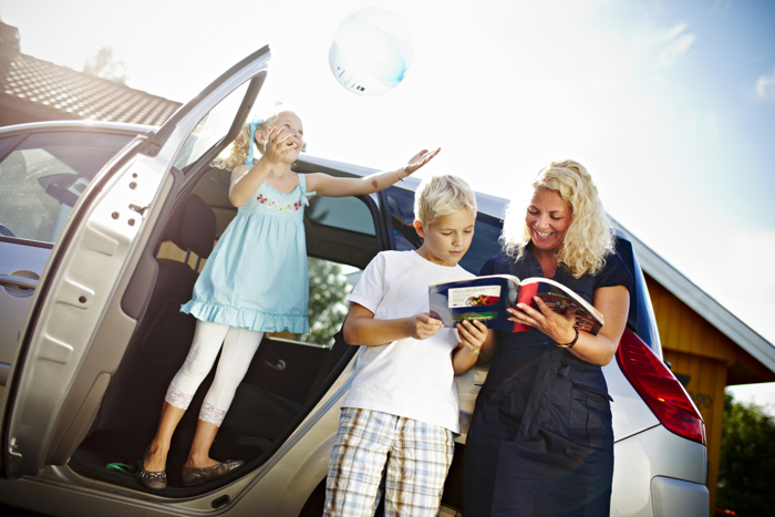 Mother and son are looking at a road map, daughter is throwing a ball in the air