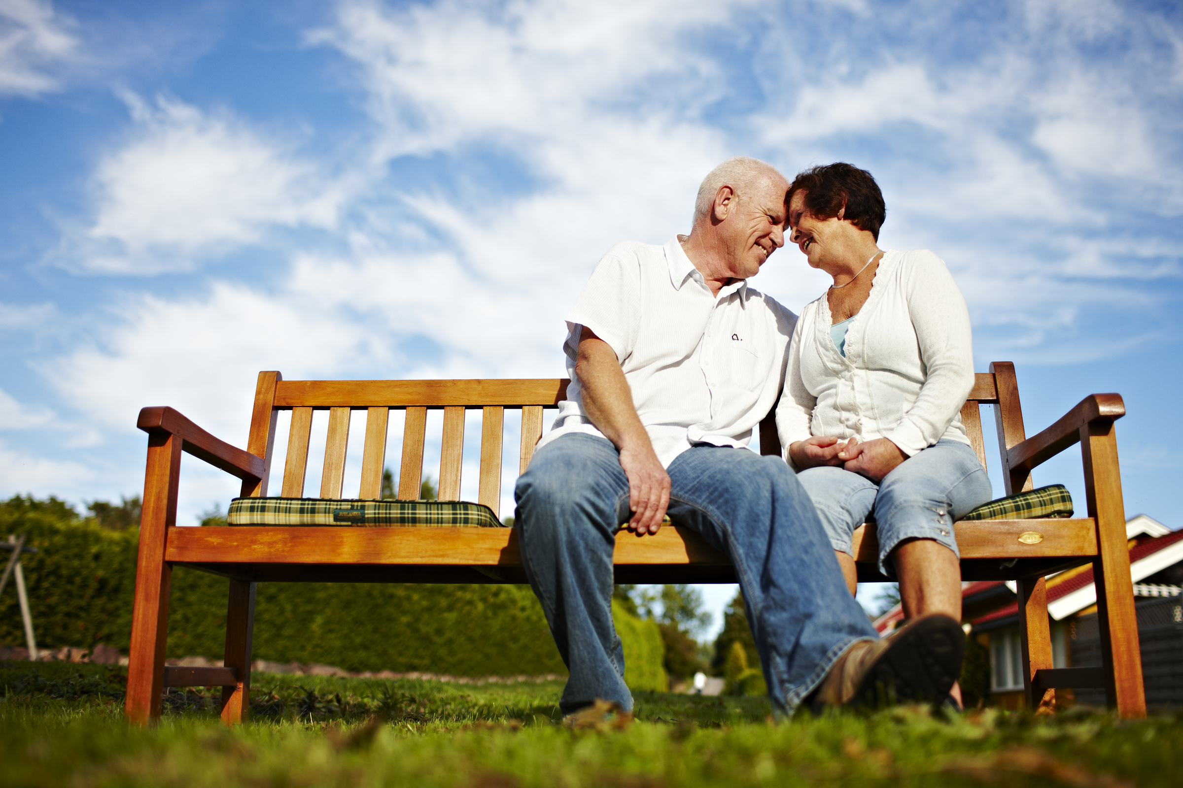 Eldre par som smiler og sitter på en benk