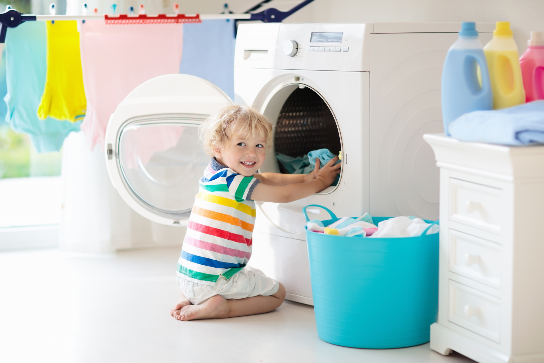 Et barn sitter foran vaskemaskin og legger inn klær 