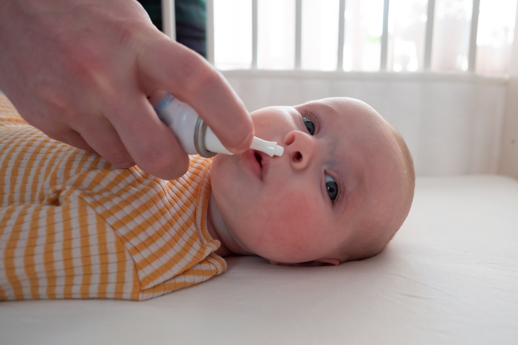 Baby som ligger på rygg, hånd til voksen som gir barnet nesespray