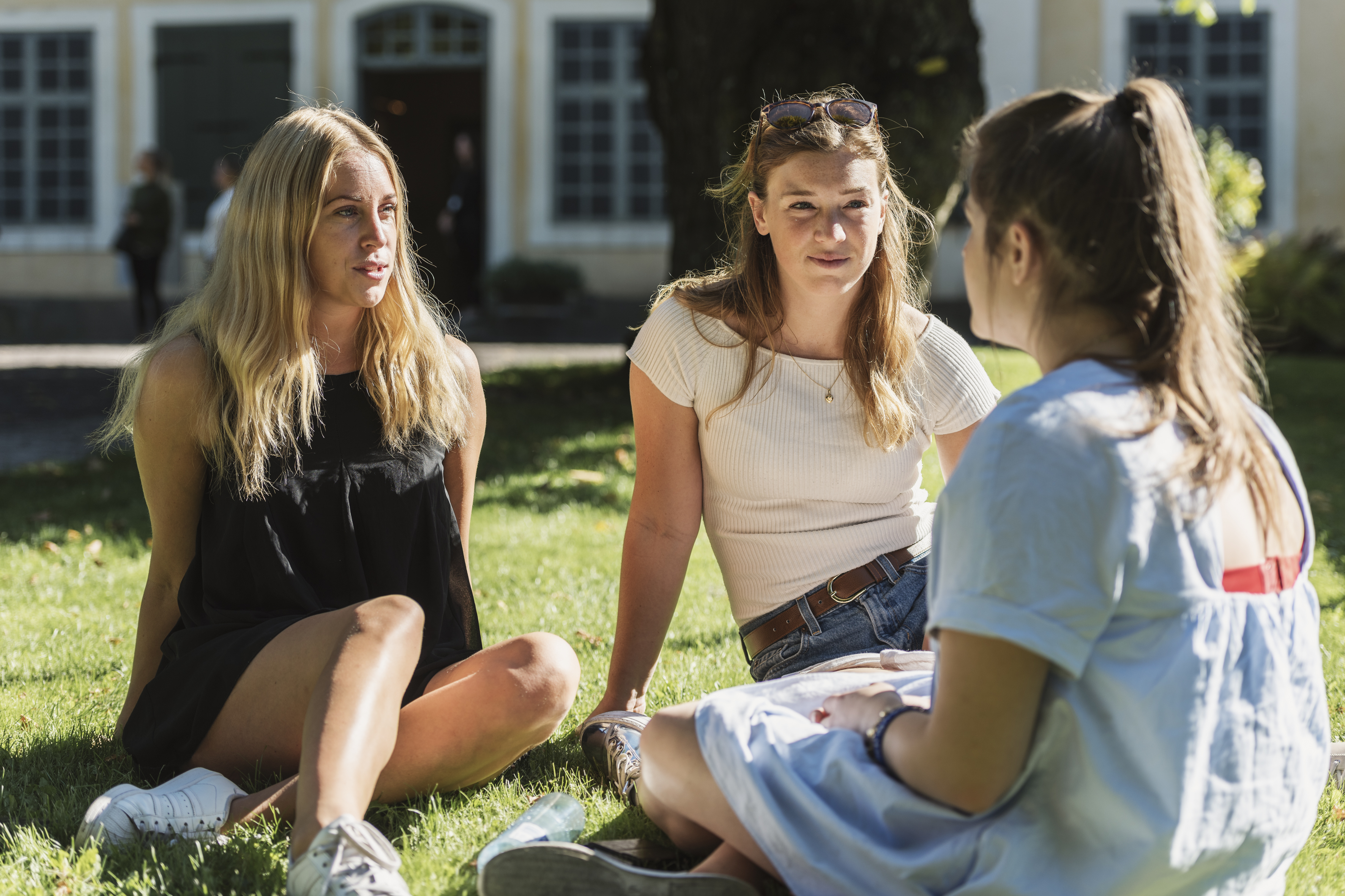 Tre unge kvinner sitter i gresset og prater