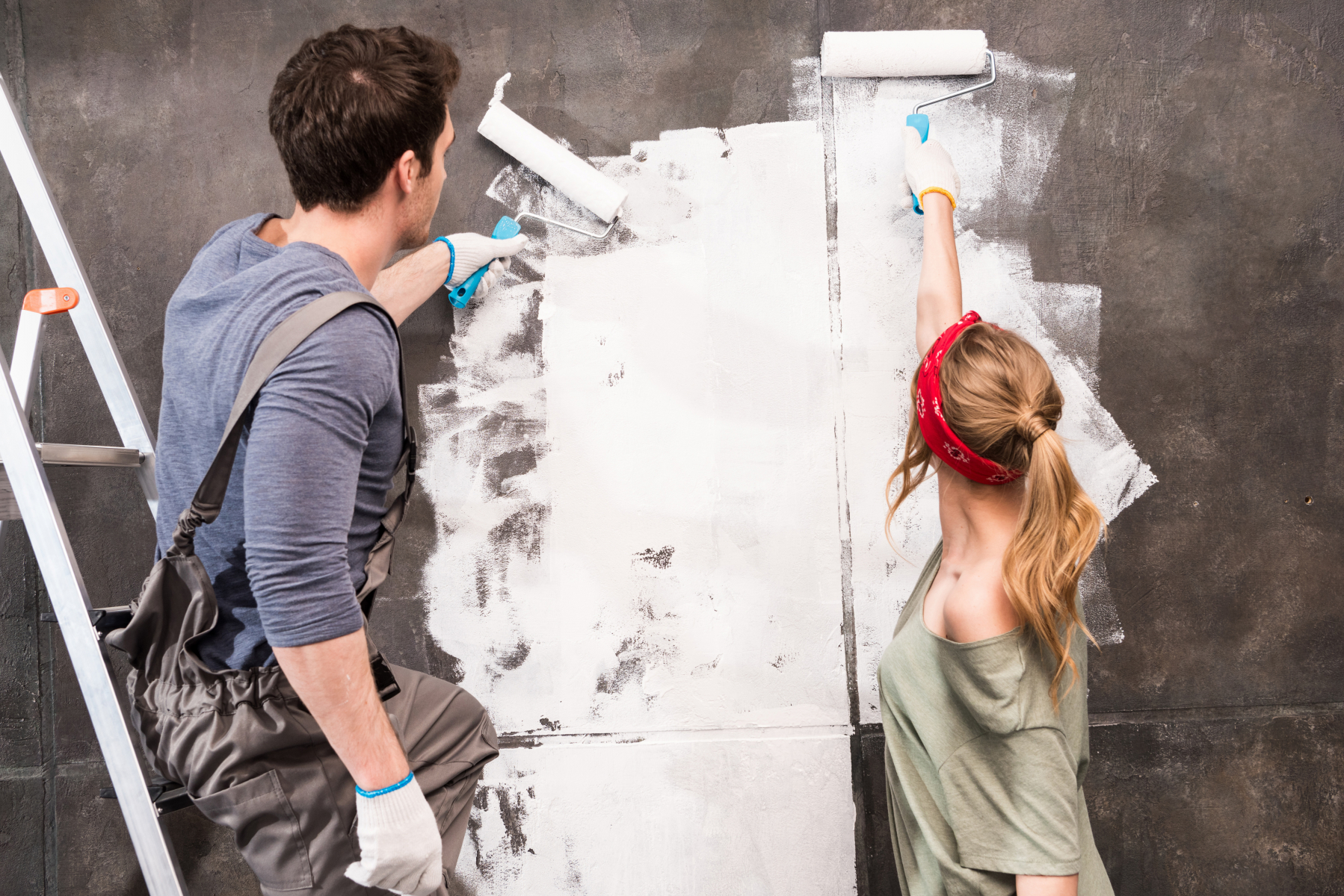 Par som sammen maler den grå veggen hvit med hver sin malingsrulle