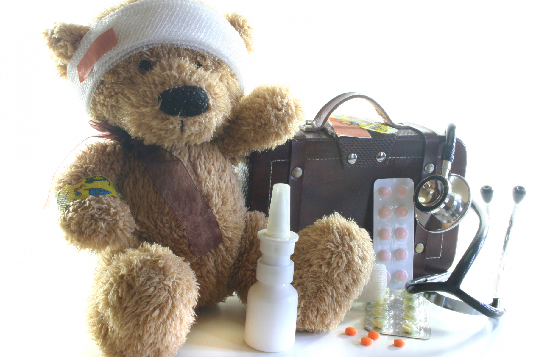 Teddy bear with a bandage on, stethoscope, medicine bag and medications