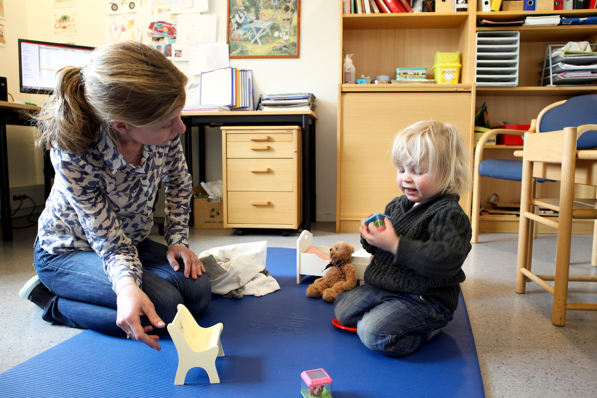 Helsesykepleier og lite barn sitter på gulvet på helsestasjonen
