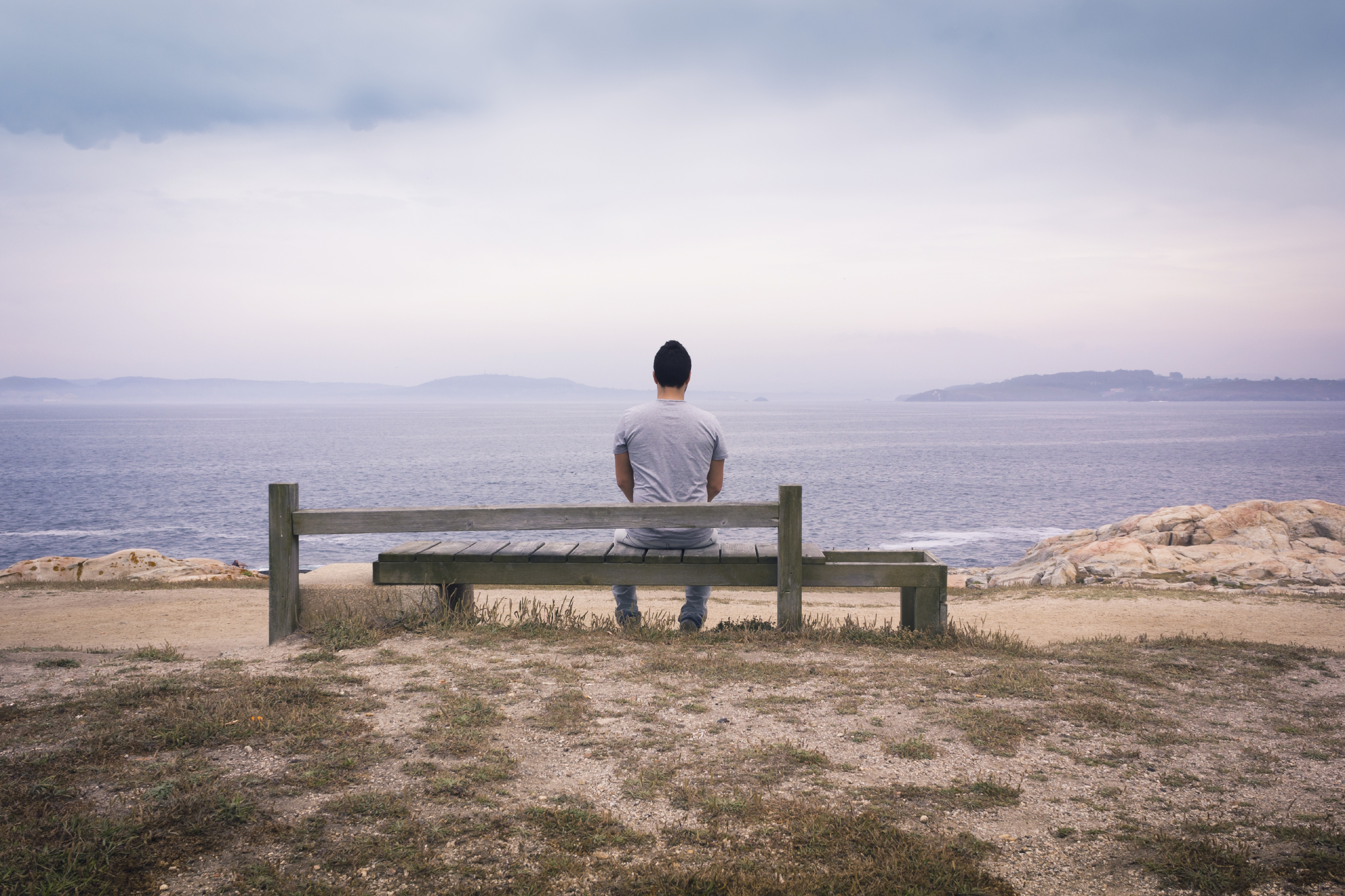 Bilde av mann som sitter på benk og ser utover havet